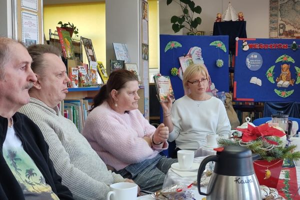 Mieszkańcy siedza i słuchaja tekstu czytanego.