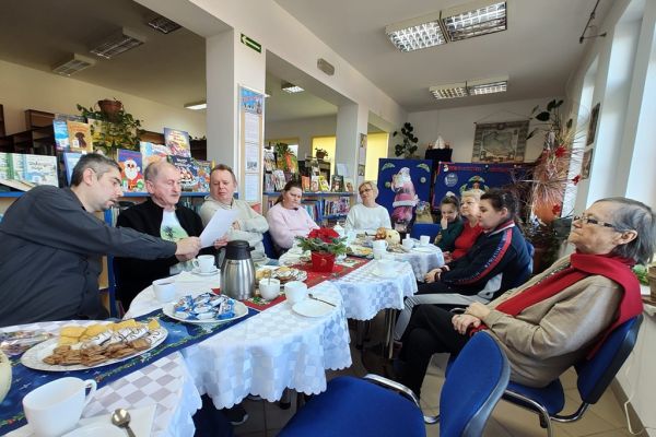 Mieszkańcy siedza i słuchaja tekstu czytanego.