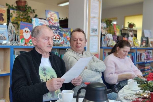 Mieszkańcy siedza i słuchaja tekstu czytanego.