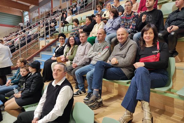 Mieszkańcy siedza na hali sportowej na widowni.