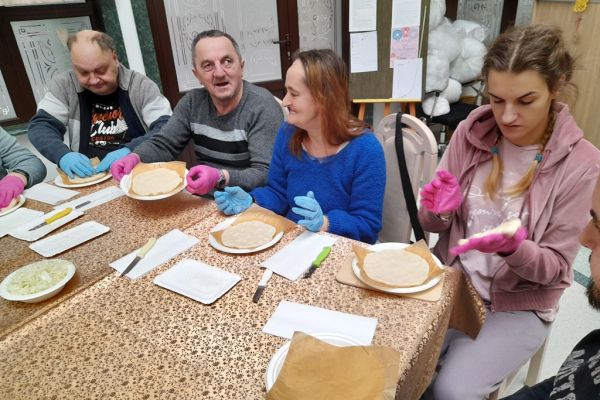 Mieszkańcy przy dużym stole  robią pizze.