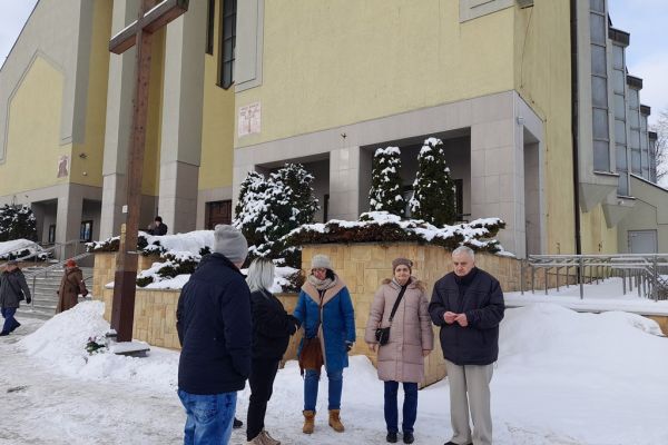 Mieszkańcy stoją przy krzyżu przed kościołem.