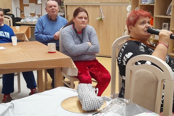 Mieszkańcy śpiewają siedząc na krzesłach.