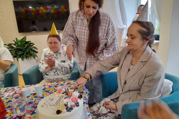 Mieszxkańcy świętują urodziny przy suto zastawionym stole. Krojenie tortu.