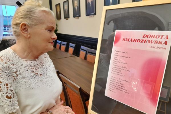 Mieszkanka stoi przy sztaludze ze swoim wierszem.