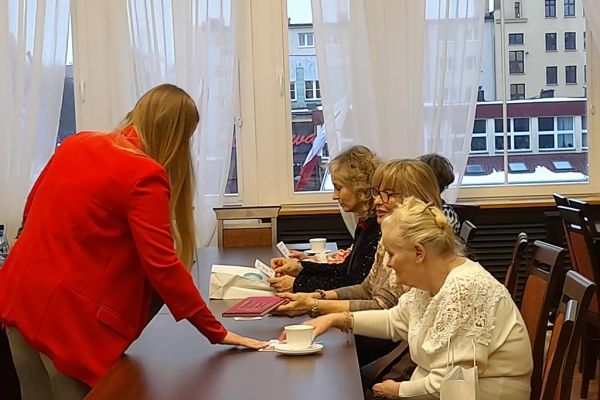 Mieszkanka otrzymuje za[proszenie siedząc przy długim stole.