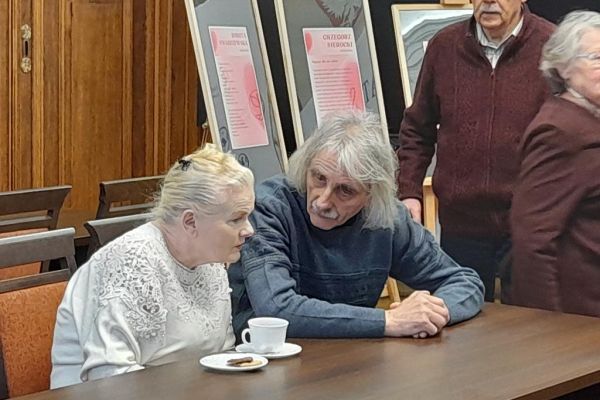 Mieszkanka rozmawia siedząc przy stole z Panem Zbigniewem.