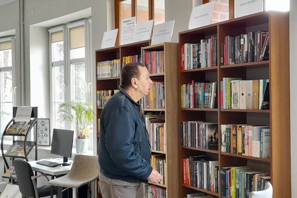 Mieszkaniec stoi przy regale w czytelni.