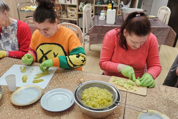 Mieszkańcy kroją produkty na słałatkę przy dużym stole.