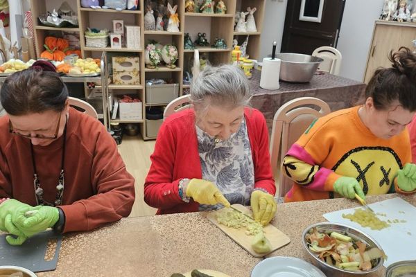 Mieszkańcy kroją produkty na słałatkę przy dużym stole.