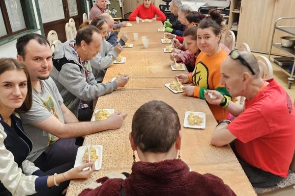 Mieszkańcy konsumują słałatkę przy dużym stole.