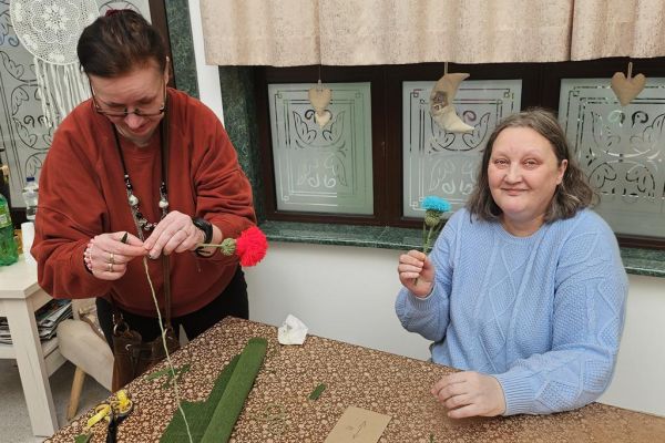 Mieszkańcy prezentują wykonane kwiaty z włóczki.