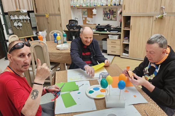 Mieszkańcy ozdabiaja kwiatkami jajka siedząc przy stolikach.