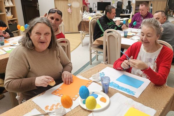 Mieszkańcy ozdabiaja kwiatkami jajka siedząc przy stolikach.