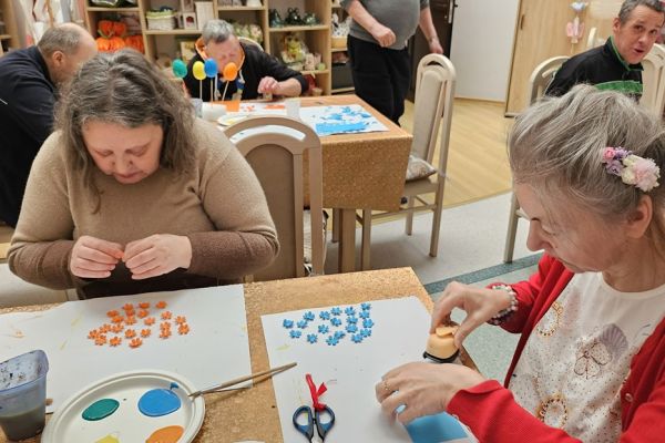 Mieszkańcy ozdabiaja kwiatkami jajka siedząc przy stolikach.