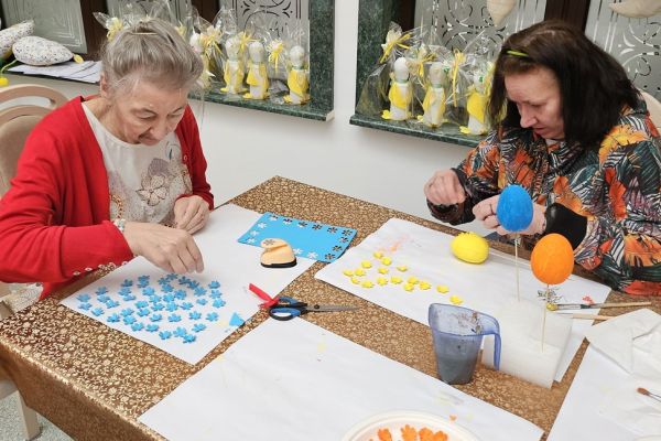 Mieszkańcy ozdabiaja kwiatkami jajka siedząc przy stolikach.