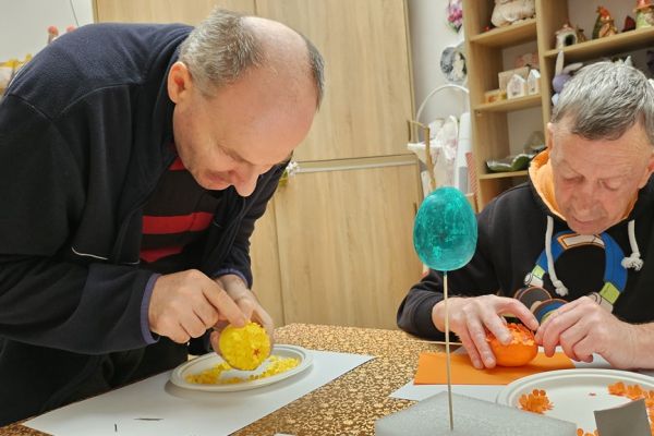 Mieszkańcy ozdabiaja kwiatkami jajka siedząc przy stolikach.