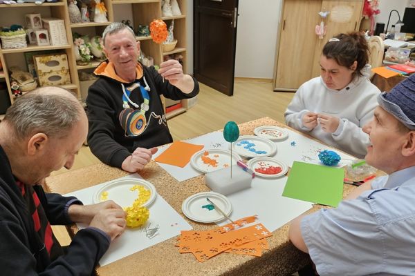 Mieszkańcy ozdabiaja kwiatkami jajka siedząc przy stolikach.