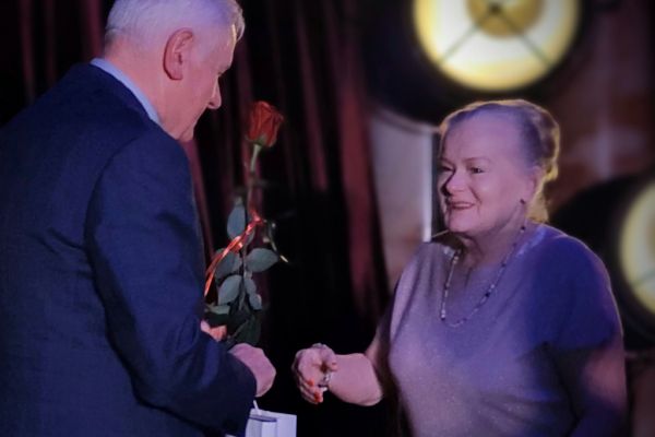 Mieszkanka odbiera podziękowanie i róże  na scenie.