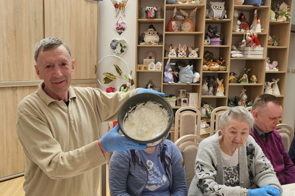 Mieszkańcy podczas zajęć mieszają ciasto na gofry przy jednym dużym stole.