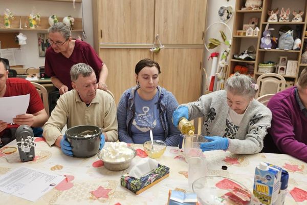Mieszkańcy podczas zajęć mieszają ciasto na gofry przy jednym dużym stole.