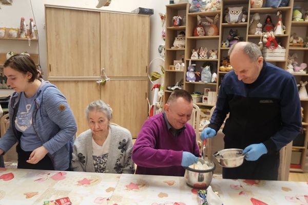 Mieszkańcy podczas zajęć mieszają ciasto na gofry przy jednym dużym stole.