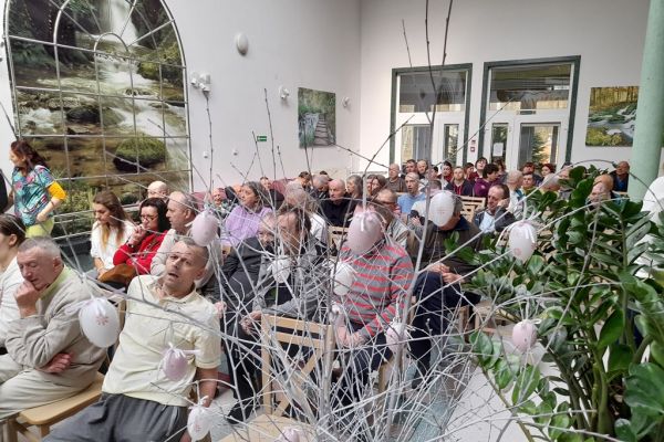 Mieszkańcy oglądfaja występ dzieci siedząc na krzesełkach w rzędach na holu.
