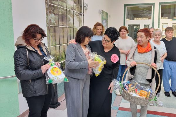Mieszkańcy  i Pani Dyrektor i Kierownik stoją na holu domu podczas kiedy Pani Wójt składa im życzenia.