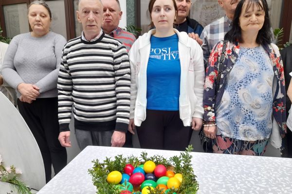 Mieszkańcy stoja przy stole z pomalowanymi jajkami w koszyczku.