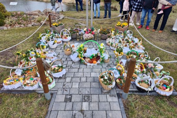 Wiele koszyczków ze święconką ułożonych pod krzyżem.