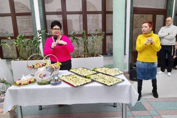 Pani Dyrektor składa mieszkańcom życzenia a przed nia stół z tacami pokrojopnych jajek.