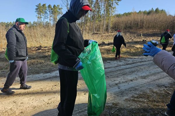 Mieszkańcy idą po lesie z workami do sprzątania.