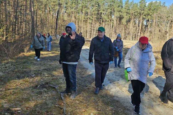 Mieszkańcy idą po lesie z workami do sprzątania.