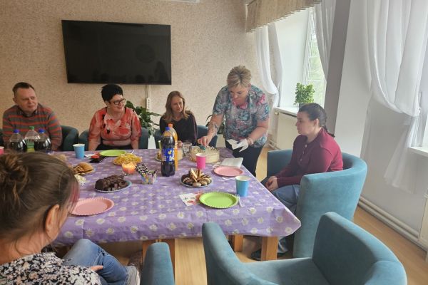 Uczestnicy urodzin siedzą przy suto zastawionym poczęstunkiem stole.