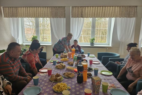 Uczestnicy urodzin siedzą przy suto zastawionym poczęstunkiem stole.