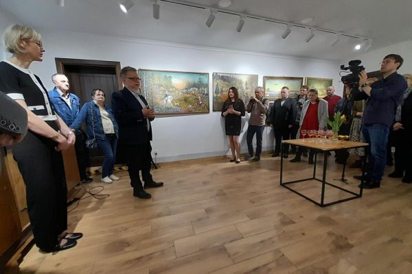 Uczestnicy wernisażu stoją wokół  sali a na ścianach wiszą obrazy.