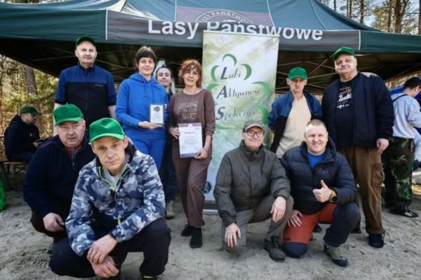 Grupowe zdjęcia mieszkańców z dyplomem za sadzenie lasu.