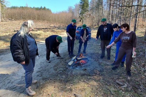 Mieszkańcy pieką kiełbaski w ognisku.
