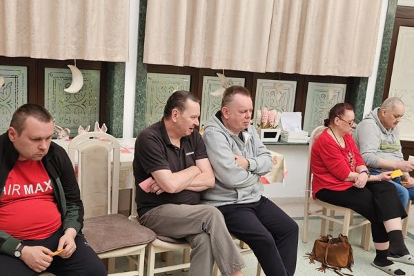 Mieszkańcy siedzą na krzesełkach w kole i odgadują piosenki.