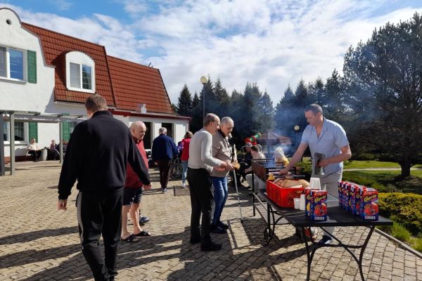 Mieszkańcy korzystają z grilla na tarasuie, grają w kręgle , częstują się kiełbaskami.