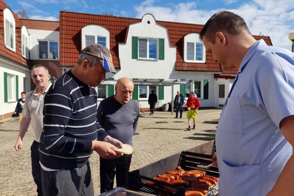 Mieszkańcy korzystają z grilla na tarasuie, grają w kręgle , częstują się kiełbaskami.