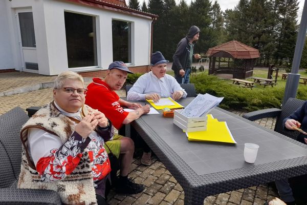 Mieszkańcy korzystają z grilla na tarasuie,tańczą, rysuja kredkami, grają w kręgle , częstują się kiełbaską.