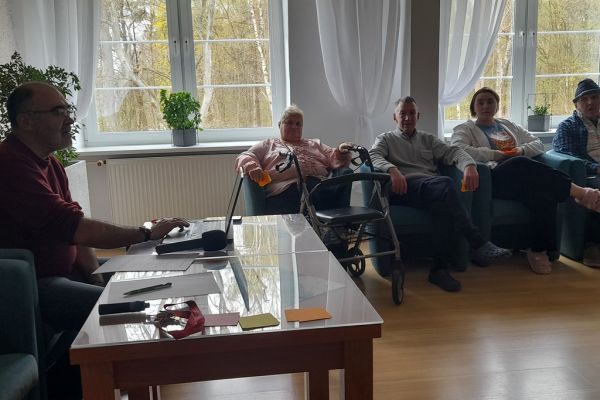Mieszkańcy siedzą w fotelach i odpowiadają na pytania prowadzącego quiz.