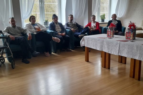 Mieszkańcy siedzą w fotelach i odpowiadają na pytania prowadzącego quiz.