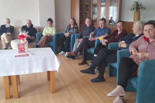 Mieszkańcy siedzą w fotelach i odpowiadają na pytania prowadzącego quiz.
