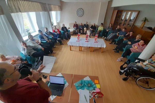 Mieszkańcy siedzą w fotelach i odpowiadają na pytania prowadzącego quiz.