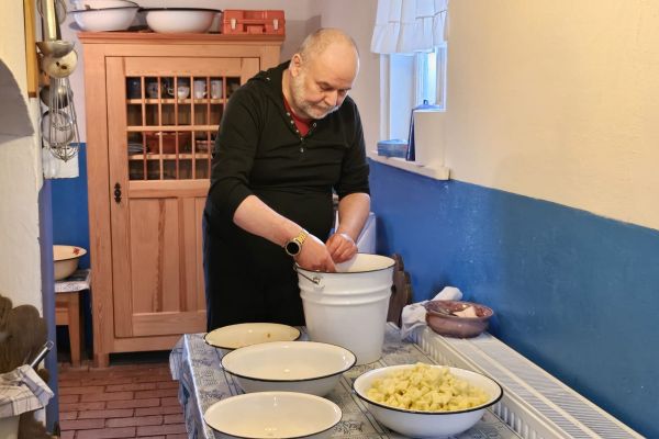 Mieszkaniec myje pokrojone warzywa w wiadrze.