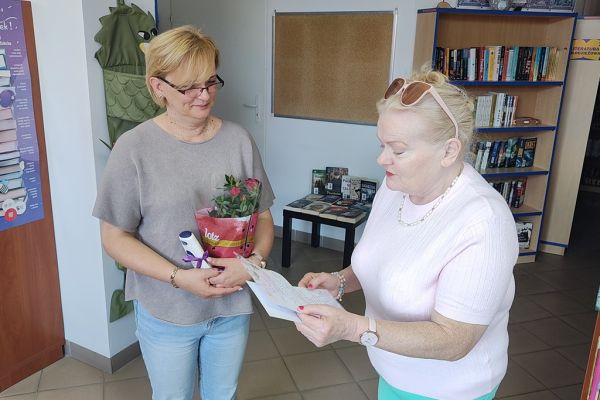 Mieszkanka czyta wiersz dla bibliotekarki, obydwie stoją.