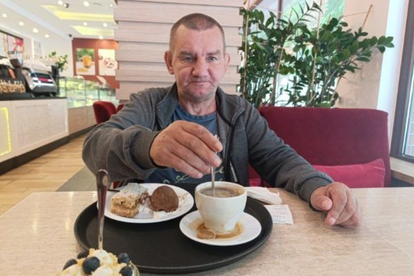 Mieszkaniec siedzi w restauracji pije kawę i je deser.