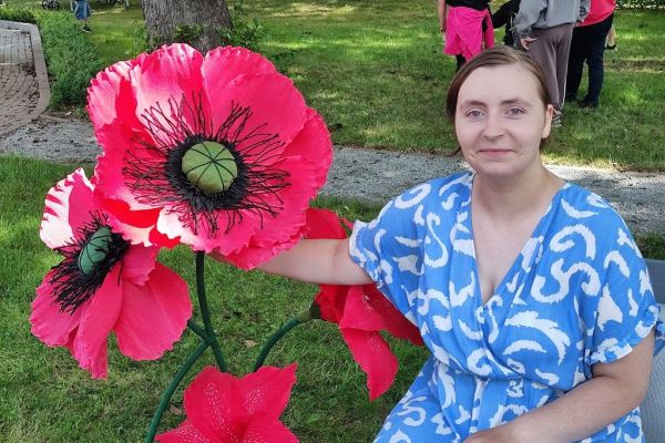 Mieszkanka na ławce z kwiatem z bibuły.